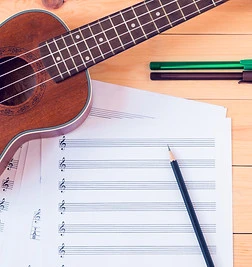 Ukulele with pen,pencil and sheet music on wooden table..jpg