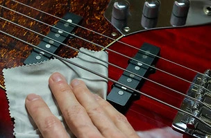 Hand on an electric bass guitar with a cleaning microfiber cloth.jpg