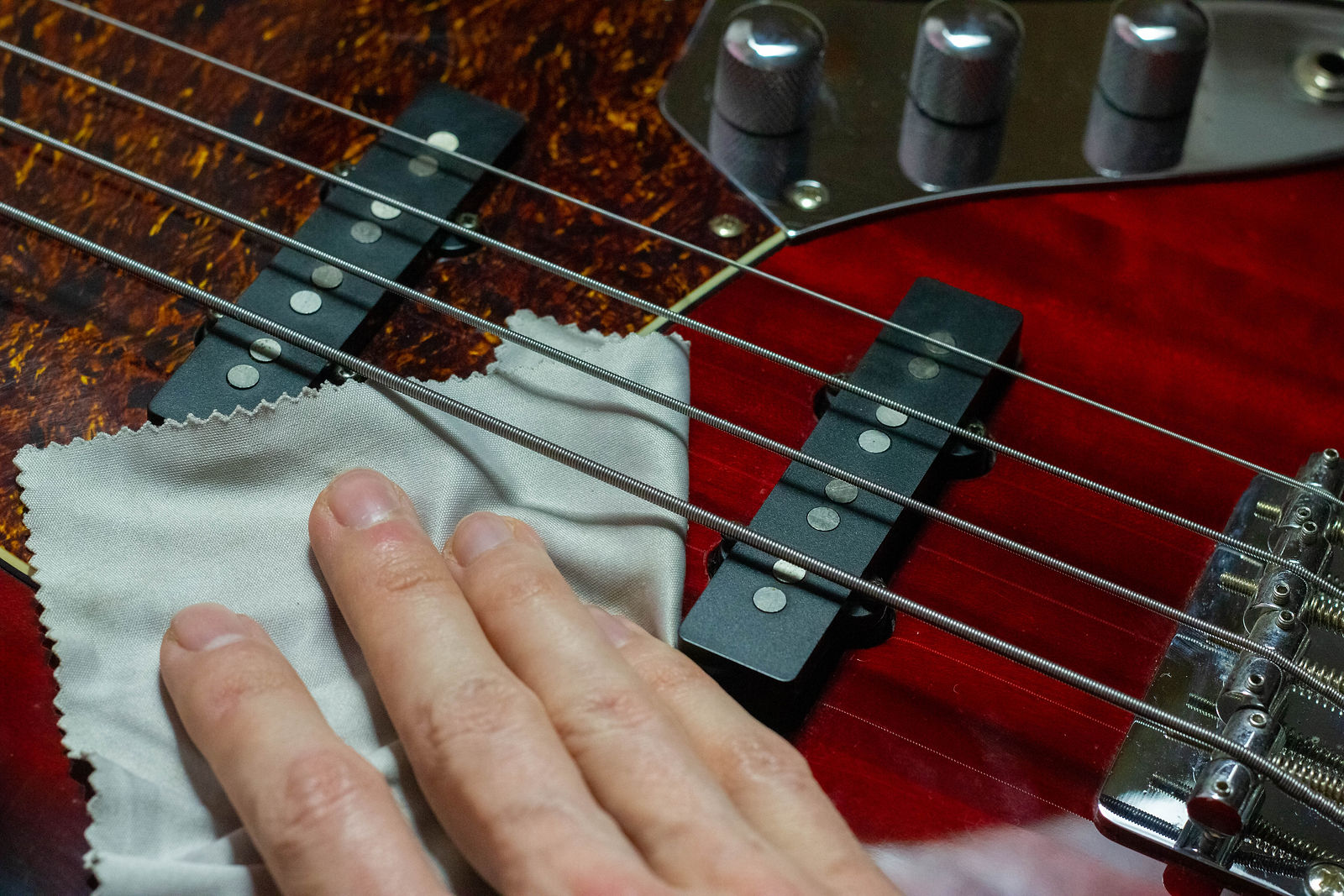 Hand on an electric bass guitar with a cleaning microfiber cloth.jpg